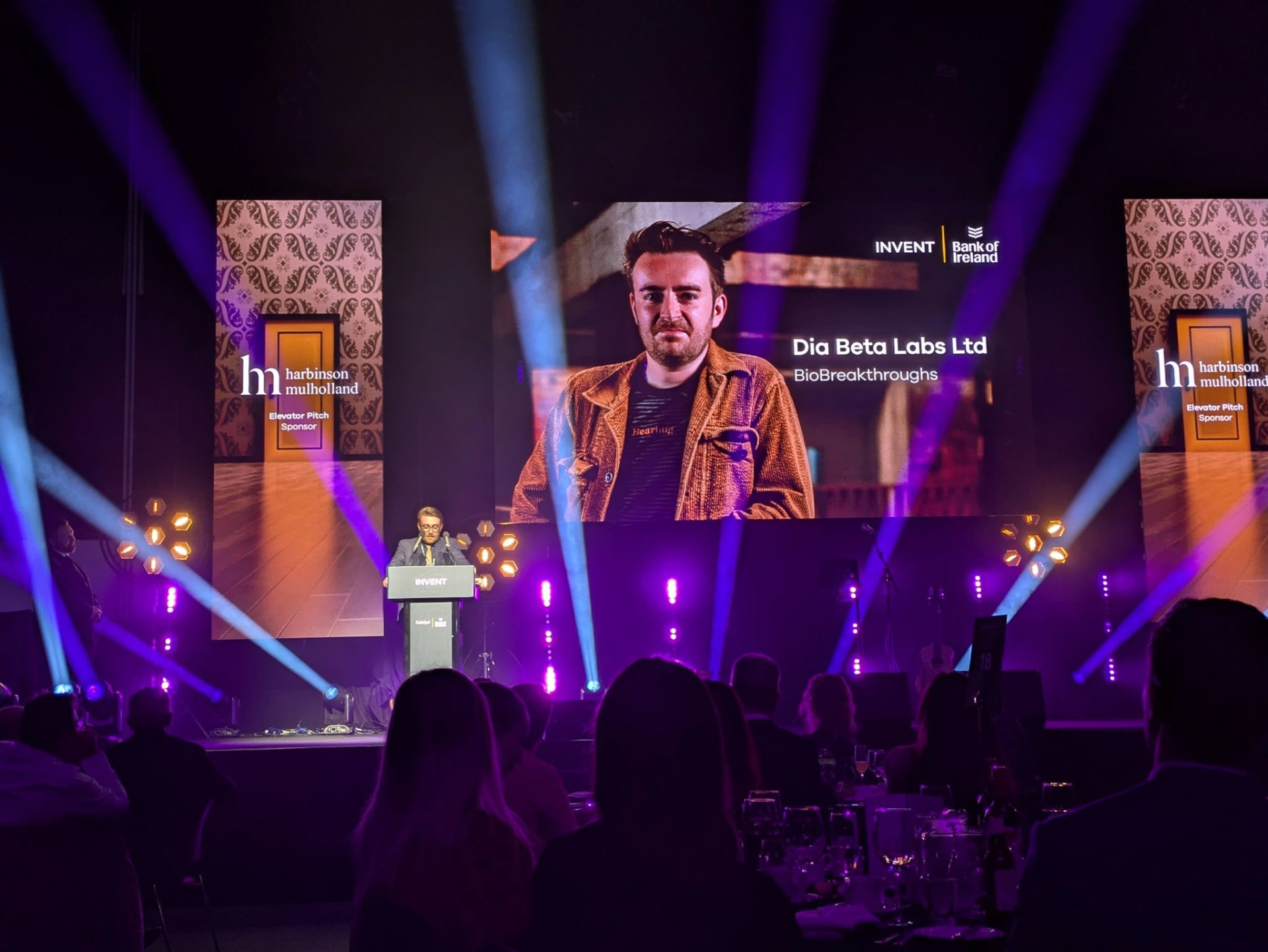 The INVENT awards stage lit in purple with a finalist on screen
