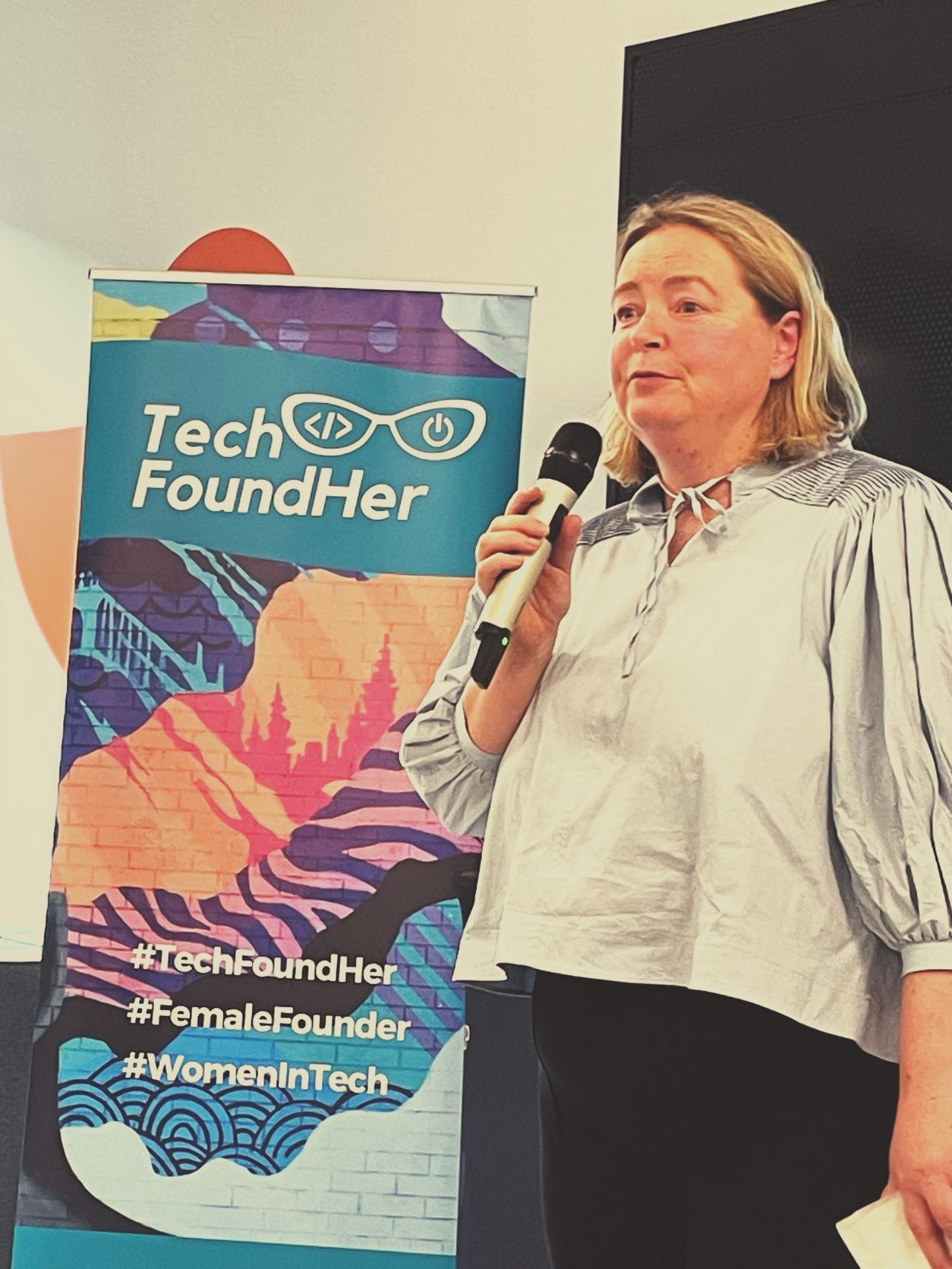 A speaker at a TechFoundHer event holding a microphone