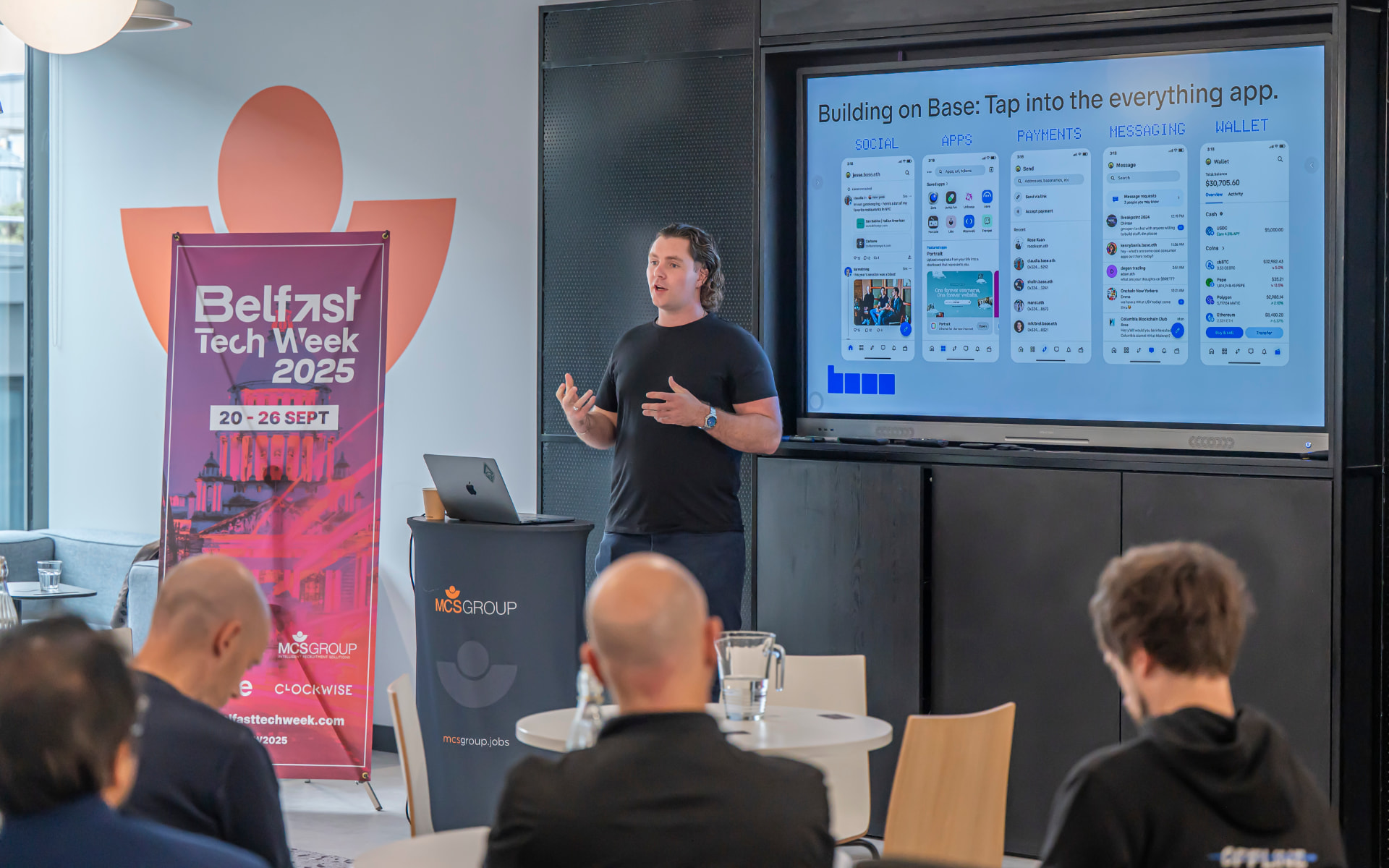 A Coinbase speaker presenting beside a Belfast Tech Week banner